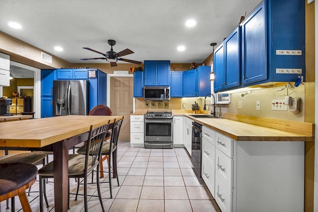 kitchen featuring stainless steel appliances, blue cabinetry, wooden counters, a sink, and light tile patterned flooring