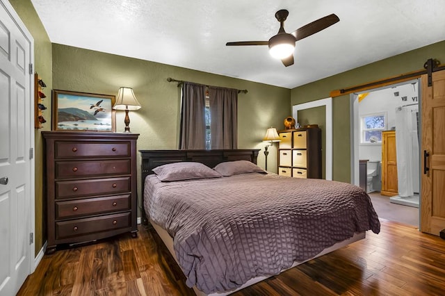 bedroom with ceiling fan, wood finished floors, a textured wall, and a barn door