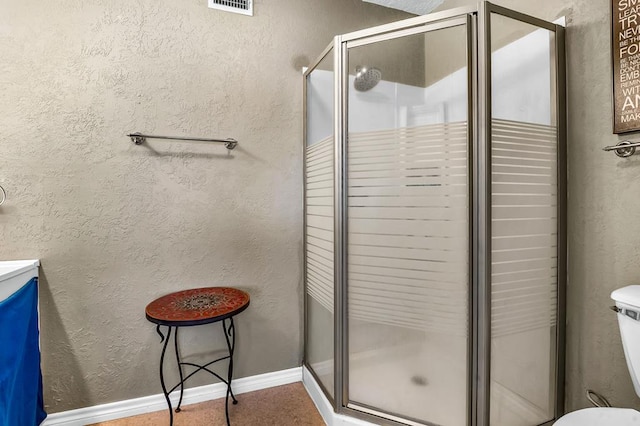 full bath featuring toilet, a shower stall, baseboards, and a textured wall