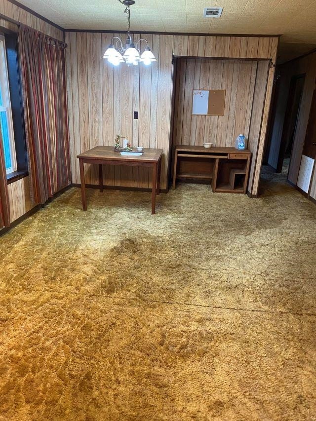 carpeted dining room featuring wooden walls, a textured ceiling, and an inviting chandelier