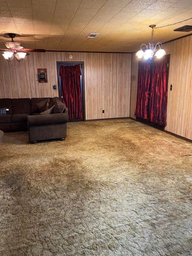 carpeted living room featuring ceiling fan with notable chandelier and wood walls