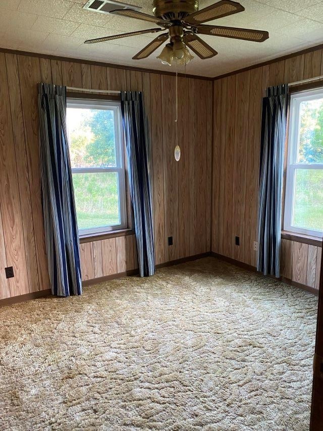 carpeted spare room with a textured ceiling, plenty of natural light, wooden walls, and ceiling fan