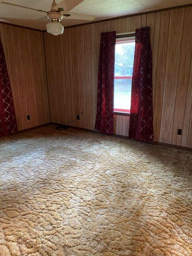 carpeted empty room with wood walls and ceiling fan