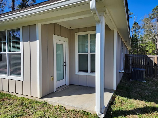 view of exterior entry featuring a patio, board and batten siding, central AC, and fence