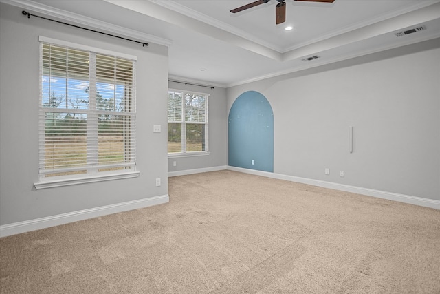 carpeted empty room with visible vents, baseboards, ornamental molding, arched walkways, and a raised ceiling