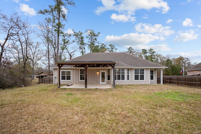 back of house with board and batten siding, fence, roof with shingles, a yard, and a patio