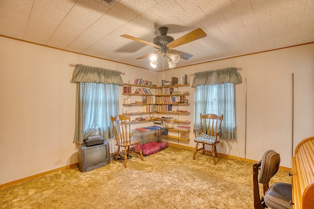 living area with ornamental molding, carpet flooring, and ceiling fan