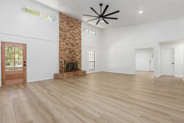 unfurnished living room featuring ceiling fan, light hardwood / wood-style flooring, a towering ceiling, and a brick fireplace