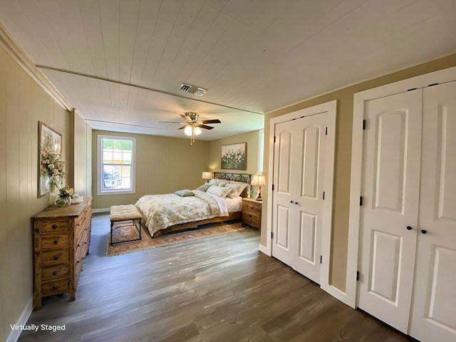 unfurnished bedroom with ceiling fan, dark hardwood / wood-style flooring, wooden walls, and multiple closets