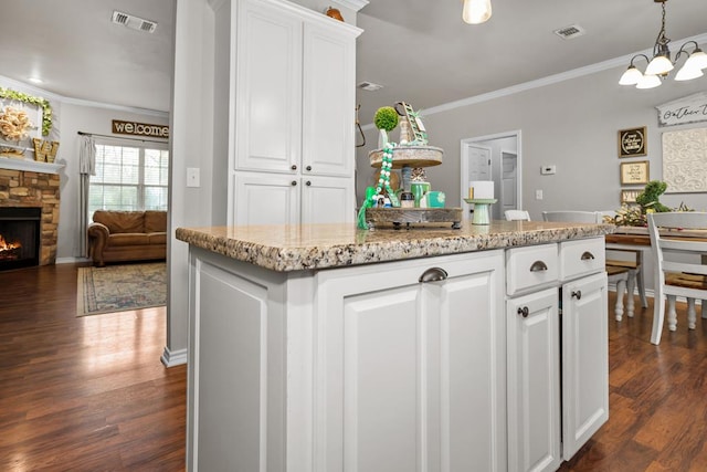 kitchen featuring visible vents, a stone fireplace, white cabinets, and crown molding