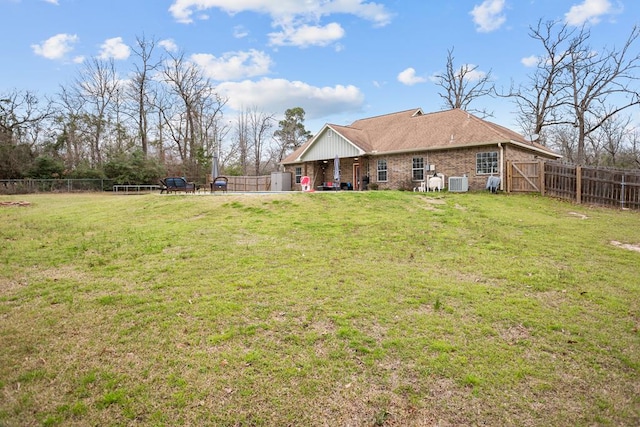 rear view of house with a yard, brick siding, central AC unit, and a fenced backyard