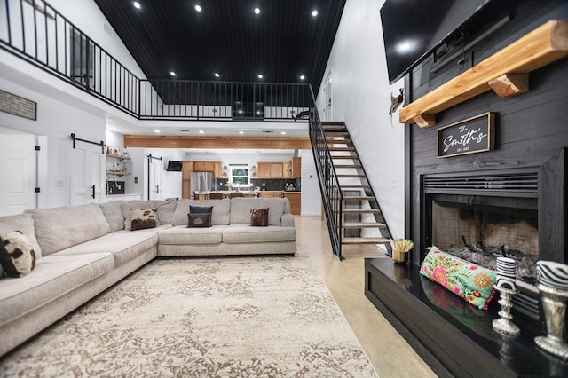 living area featuring stairway, finished concrete floors, a barn door, a fireplace, and a towering ceiling