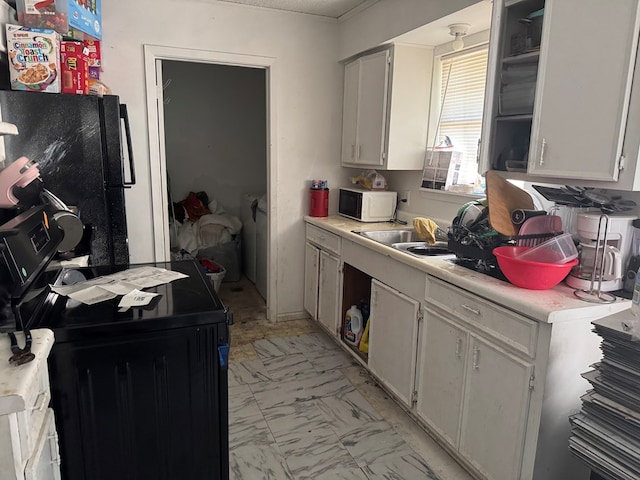 kitchen with black refrigerator, white cabinetry, and sink