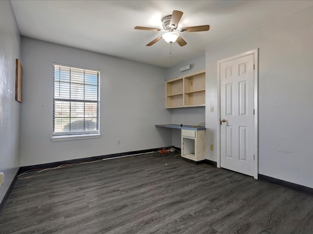 unfurnished office featuring baseboards, dark wood-type flooring, a ceiling fan, and built in study area