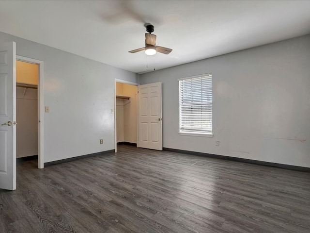 unfurnished bedroom with a spacious closet, baseboards, and dark wood-style flooring