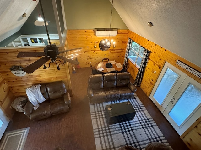 living room with wooden walls, ceiling fan, a textured ceiling, and high vaulted ceiling