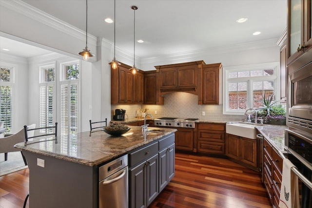 kitchen featuring appliances with stainless steel finishes, ornamental molding, dark wood-type flooring, and an island with sink