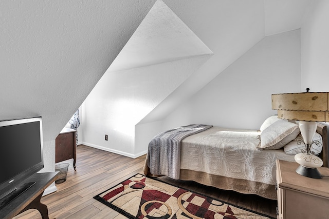 bedroom featuring hardwood / wood-style flooring, vaulted ceiling, and a textured ceiling