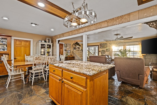 kitchen featuring ceiling fan with notable chandelier, light stone countertops, a healthy amount of sunlight, and a kitchen island