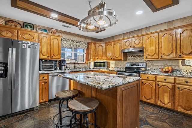 kitchen featuring a kitchen island, appliances with stainless steel finishes, tasteful backsplash, sink, and light stone counters