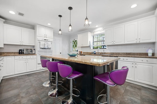 1514 Spanish Moss Dr, Lufkin, TX 75904 - kitchen featuring double oven, a breakfast bar, white cabinets, a center island, and light stone counters