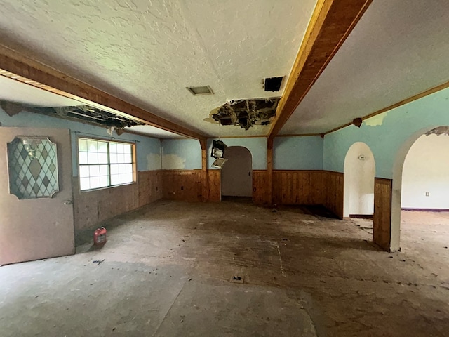 empty room with wood walls, arched walkways, and wainscoting