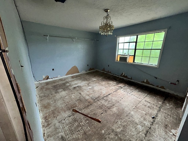 empty room featuring cooling unit, an inviting chandelier, and a textured ceiling