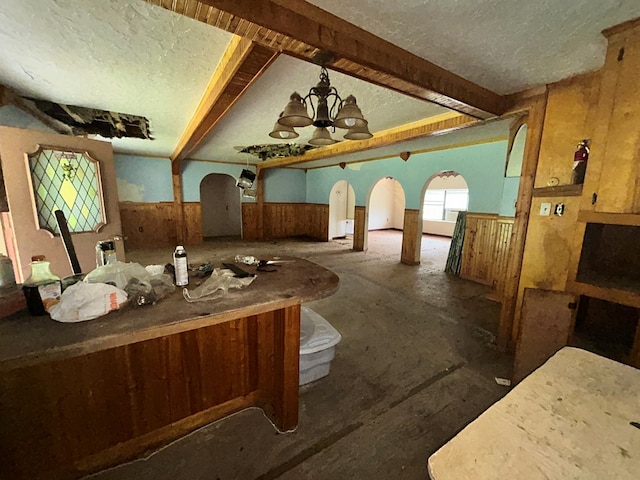 interior space featuring a textured ceiling, beamed ceiling, a notable chandelier, and a wainscoted wall