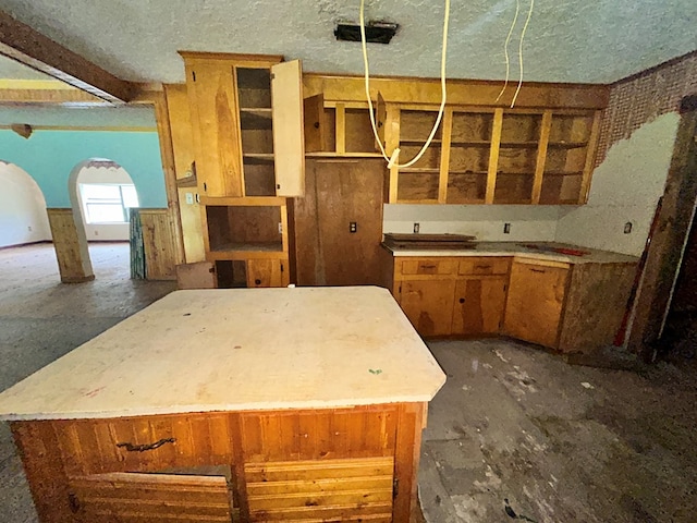 kitchen featuring arched walkways, brown cabinets, a textured ceiling, and a kitchen island