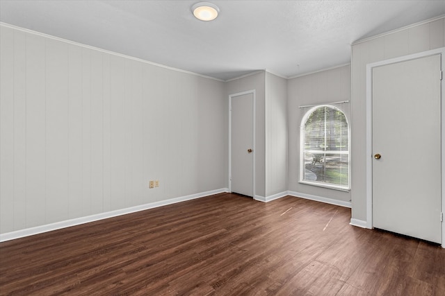 spare room featuring a textured ceiling, wooden walls, dark hardwood / wood-style floors, and ornamental molding