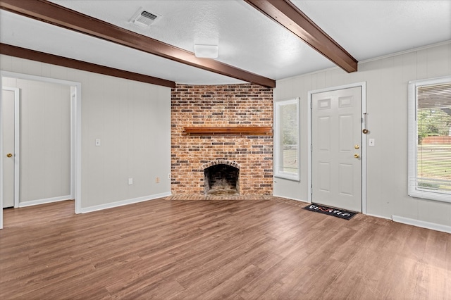 unfurnished living room featuring a fireplace, beamed ceiling, wood-type flooring, and a textured ceiling