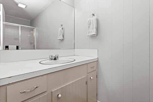 bathroom with wooden walls, vanity, a shower with shower door, and ornamental molding