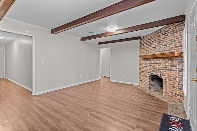 unfurnished living room featuring a brick fireplace, beamed ceiling, a textured ceiling, and light wood-type flooring