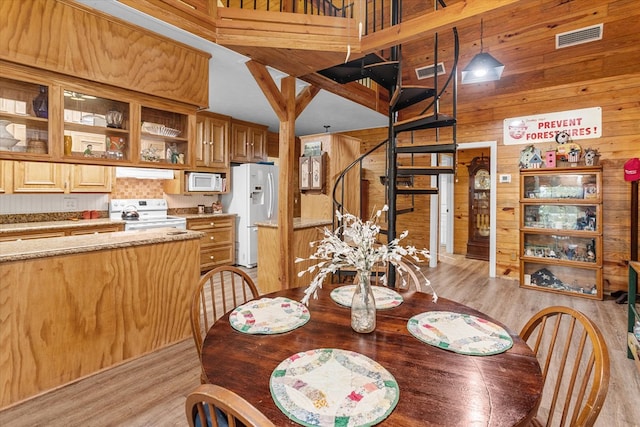 dining space featuring a towering ceiling, light hardwood / wood-style flooring, and wood walls