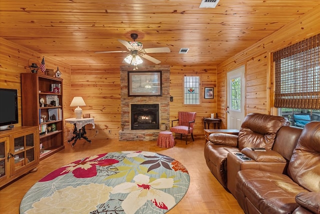 living room featuring ceiling fan, a stone fireplace, wooden ceiling, and wooden walls