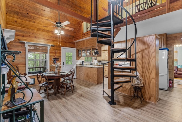 dining room with beam ceiling, ceiling fan, high vaulted ceiling, wood walls, and light wood-type flooring