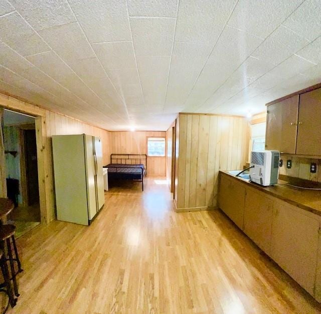 interior space featuring stainless steel fridge, wooden walls, and light wood-type flooring