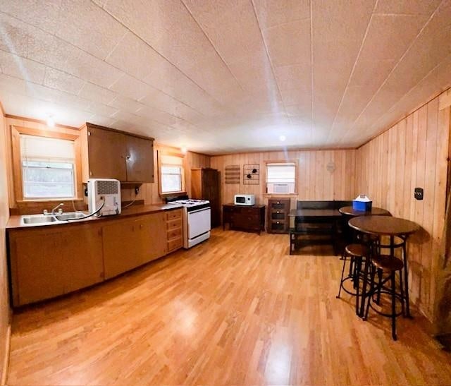 kitchen with white appliances, sink, wooden walls, light hardwood / wood-style floors, and kitchen peninsula