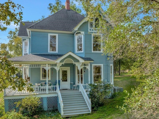 victorian house featuring a porch, central air condition unit, and a front yard