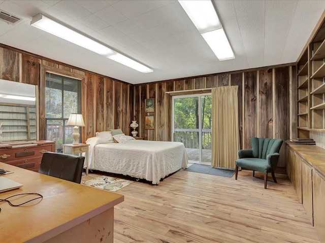 bedroom with access to outside, wooden walls, and light hardwood / wood-style flooring