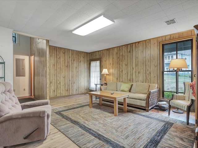 living room featuring wood walls, electric panel, and light hardwood / wood-style flooring