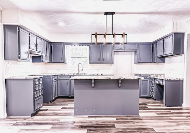 kitchen with tasteful backsplash, gray cabinets, a center island, light wood-type flooring, and pendant lighting