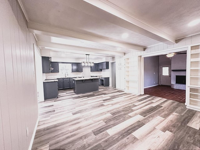 kitchen with light countertops, open floor plan, light wood-type flooring, a kitchen island, and beamed ceiling