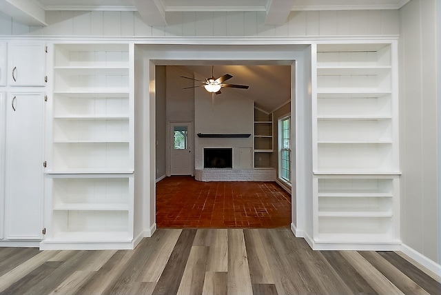 unfurnished living room featuring ceiling fan, a brick fireplace, built in features, baseboards, and wood finished floors