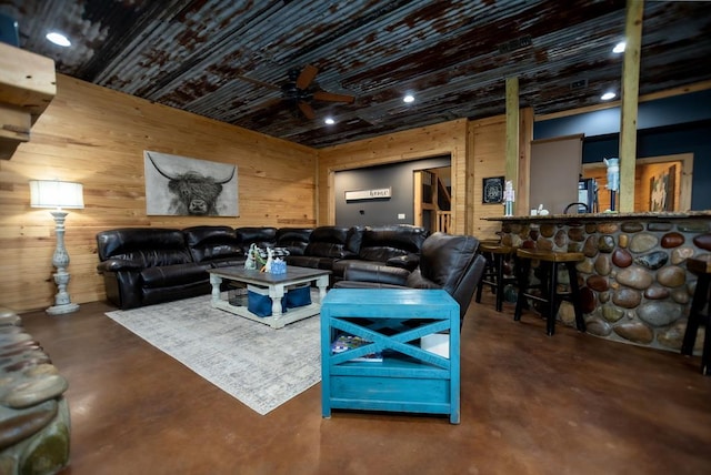 living room with a ceiling fan, wooden walls, and finished concrete flooring