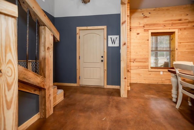 foyer with wooden walls, baseboards, and concrete floors