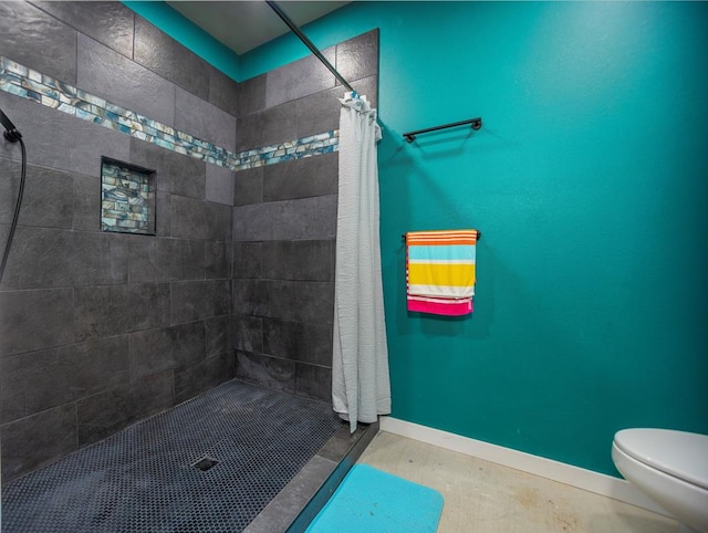 full bathroom with baseboards, tiled shower, and toilet