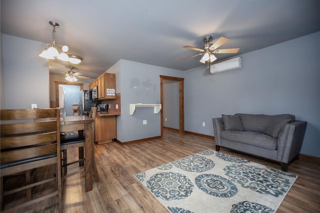 living area featuring ceiling fan with notable chandelier, an AC wall unit, wood finished floors, and baseboards