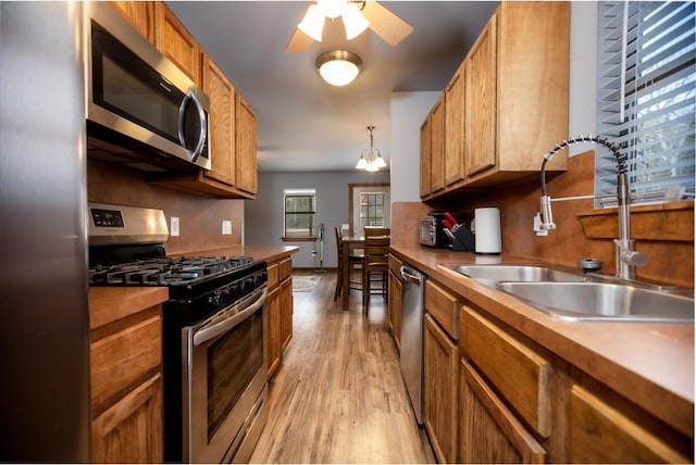 kitchen featuring light wood finished floors, decorative backsplash, brown cabinets, stainless steel appliances, and a sink