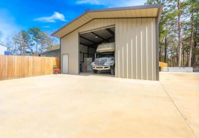 view of pole building featuring concrete driveway and fence